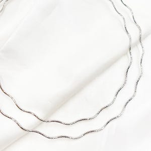 May include: A silver chain necklace with three strands of delicate, wavy links.