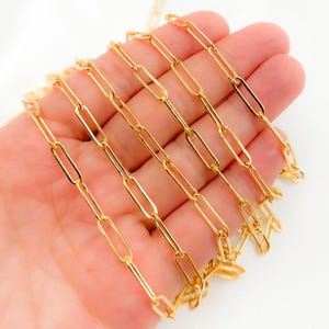 Puede incluir: Cadena dorada con forma rectangular enlazada. La cadena es de metal y tiene un acabado brillante.