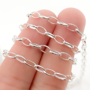May include: Close-up of a silver-colored chain with oval links. The chain is held in a person's hand, with the links appearing bright and reflective. The chain is likely used for jewelry or crafting.