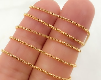 May include: Close-up of a gold chain necklace with a box chain design. The chain is shown in multiple lengths, draped over a finger.