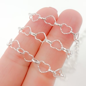 May include: Three silver heart-shaped chains, each with a different length, are displayed on a finger.