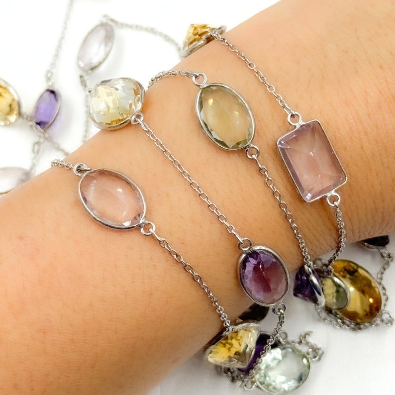 May include: A silver chain bracelet with multiple gemstone charms. The charms are in various shapes and colors, including clear, light pink, light green, and purple.