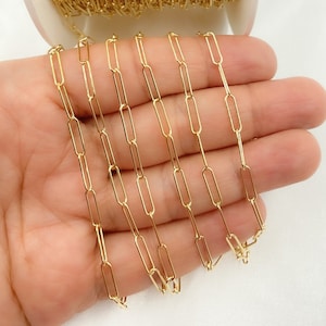 May include: A gold-colored chain made of small, rectangular links. The chain is lying on a hand, with several strands of the chain visible.