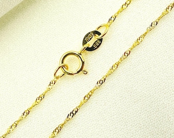 May include: Close-up of a gold-colored necklace with a delicate chain design. The necklace features a lobster clasp and a small tag with text. The chain has a twisted rope pattern. The background is a light, neutral color.