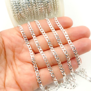 May include: Four strands of silver curb chain, a popular style of chain, are laid out on a hand. The chain is flat and has a slightly rounded edge.
