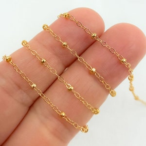 May include: Gold chain with small round beads. The chain is shown in three lengths.