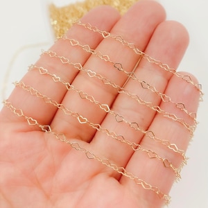 Puede incluir: Delicada cadena dorada con un diseño repetido en forma de corazón. La cadena se sostiene en una mano, mostrando sus intrincados detalles y el cálido tono metálico. Ideal para la fabricación de joyas o para añadir un toque romántico a las manualidades.