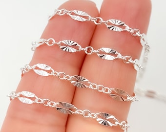 May include: Four silver chains with a diamond-shaped pattern. The chains are layered on top of each other and are held in a hand.