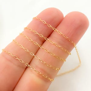 May include: A close-up of a gold chain necklace. The chain is made of small, oval-shaped links. The chain is lying on a person's fingers.