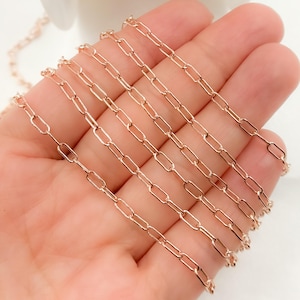 May include: A close-up of a rose gold chain with a delicate, oval-shaped link. The chain is laid out in a straight line on a hand, showing the intricate detail of the links.