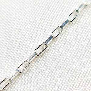 May include: A silver chain necklace with a box chain design. The chain is made of small, rectangular links.