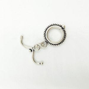 May include: Silver-toned metal clasp with a decorative circle and a hook. The clasp is designed for attaching jewelry or other items.
