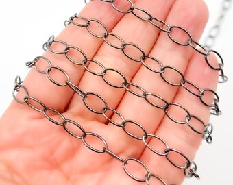 Op de afbeelding: Close-up van een gunmetal-kleurige ketting met ovale schakels. De ketting wordt weergegeven op een lichte achtergrond. De schakels zijn gelijkmatig verdeeld en creëren een lineair patroon. Deze ketting is geschikt voor het maken van sieraden en andere knutselprojecten.