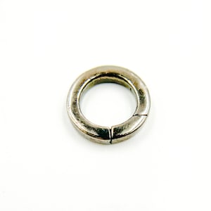 May include: A silver-colored, circular clasp with a hinged opening. The clasp is made of metal and has a slightly worn appearance. The design is simple and functional, suitable for various jewelry or craft projects.
