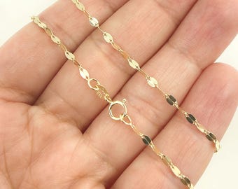 Puede incluir: Un delicado collar de color dorado con un diseño único de eslabones ovalados aplanados. El collar se muestra con un cierre de mosquetón y se sostiene en una mano, mostrando sus finos detalles. La cadena mide aproximadamente 45 cm de largo.