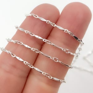 May include: Four silver chains of different lengths, each with a delicate, flat, and slightly curved link design.