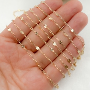 May include: Delicate gold-colored chain necklace featuring a repeating pattern of small, flat, circular charms interspersed with elongated links. The necklace has a bright, reflective surface, suggesting a polished finish. The design is simple yet elegant, suitable for layering or standalone wear.
