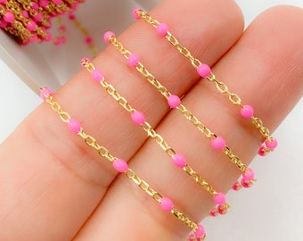 May include: Close-up of a gold-colored chain with small, bright pink beads. The chain is made of small, rectangular links. The beads are evenly spaced along the chain. The chain is shown against a light background.