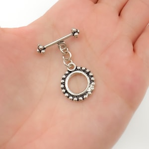 May include: Silver barbell with a small chain and a round charm with a beaded edge.
