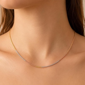 Puede incluir: Un delicado collar con un diseño tricolor. El collar presenta secciones de oro, plata y oro rosa, creando un efecto sutil pero llamativo. La cadena es fina y parece estar hecha de pequeñas cuentas conectadas. El collar se lleva alrededor del cuello.
