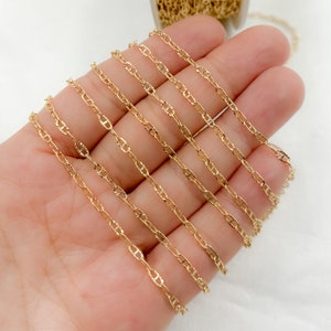 May include: A close-up of a hand holding multiple strands of gold-colored chain. The chain is a delicate, rope-like style with a slightly textured finish.
