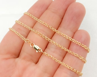 May include: A gold-colored chain necklace with a wheat-style design. The necklace is shown on a hand, with the clasp visible. The chain is made of small, interconnected links, creating a textured appearance. The background is a plain white surface.