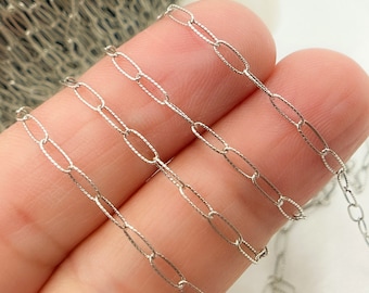 May include: Close-up of a silver chain with oval links. The chain is made of small, delicate links that are connected together to form a continuous loop.