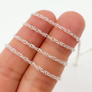 May include: Silver chain necklace with a twisted rope design. The chain is shown in multiple layers on a finger.