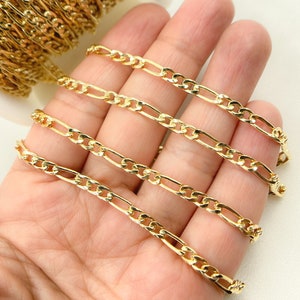 May include: Four gold-colored chains of different lengths, likely made of metal, are displayed on a hand. The chains are all the same style, with a flat, oval-shaped link.
