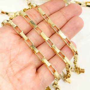 May include: Three gold chains with a box link design. The chains are laid out on a hand, showing the detail of the links.