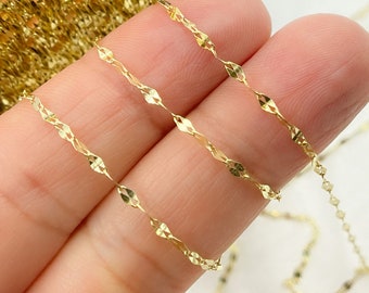 May include: Three strands of gold chain with a diamond-shaped pattern. The chain is delicate and has a subtle shimmer.