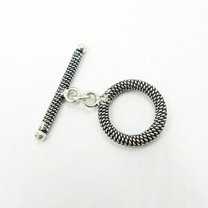 May include: Silver toggle clasp with a twisted design. The clasp has a round ring and a bar with a small loop.
