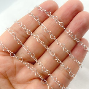 May include: Silver heart chain, a delicate and dainty chain with a heart-shaped link design. The chain is shown in multiple strands, highlighting its intricate detail.