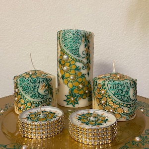May include: Set of five candles with green and gold henna designs. The larger candles are pillar candles and the smaller candles are tea lights. The tea lights have a gold glitter band around the bottom.