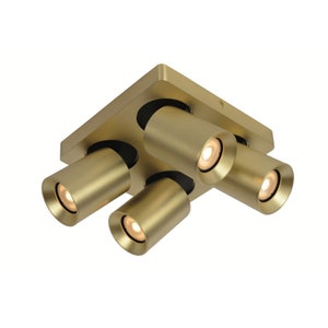 Può includere: Un apparecchio di illuminazione a soffitto dorato con quattro faretti orientabili. L'apparecchio ha una base quadrata e i faretti sono cilindrici.