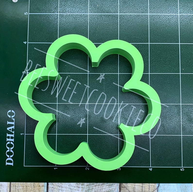 Pu&ograve; includere: Tagliapasta verde brillante a forma di quadrifoglio. Il tagliapasta &egrave; realizzato in plastica e ha un bordo liscio e arrotondato. Il testo "BEES SWEET COOKIES" &egrave; scritto sull'immagine.