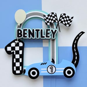 May include: A cake topper featuring the name BENTLEY in black letters with a light blue outline. It includes a large number one with a black and white checkered pattern, a light blue race car with the number one, two checkered flags, and a balloon.