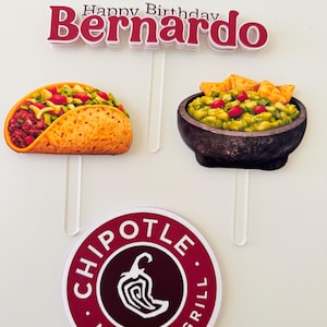 May include: Cake toppers with a Mexican food theme. Includes a taco, guacamole, and a Chipotle Mexican Grill logo. The top topper reads "Happy Birthday Bernardo" in red and white.