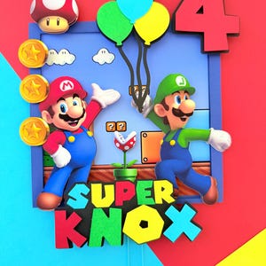 May include: A colorful cake topper featuring Mario and Luigi characters, gold coins, a mushroom, and balloons. The number 4 is displayed, along with the text "SUPER KNOX". The background is a mix of red, blue, and yellow.