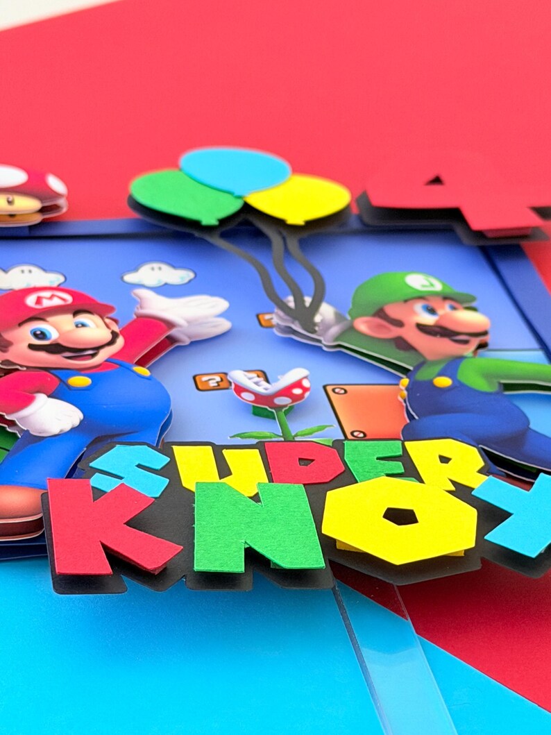May include: A colorful pop-up card featuring Mario and Luigi characters. The card has a blue background with the words "SUPER KNOX" in large, multi-colored letters. Mario is wearing a red hat and blue overalls, while Luigi is in a green hat and overalls. Balloons and a mushroom are also visible.