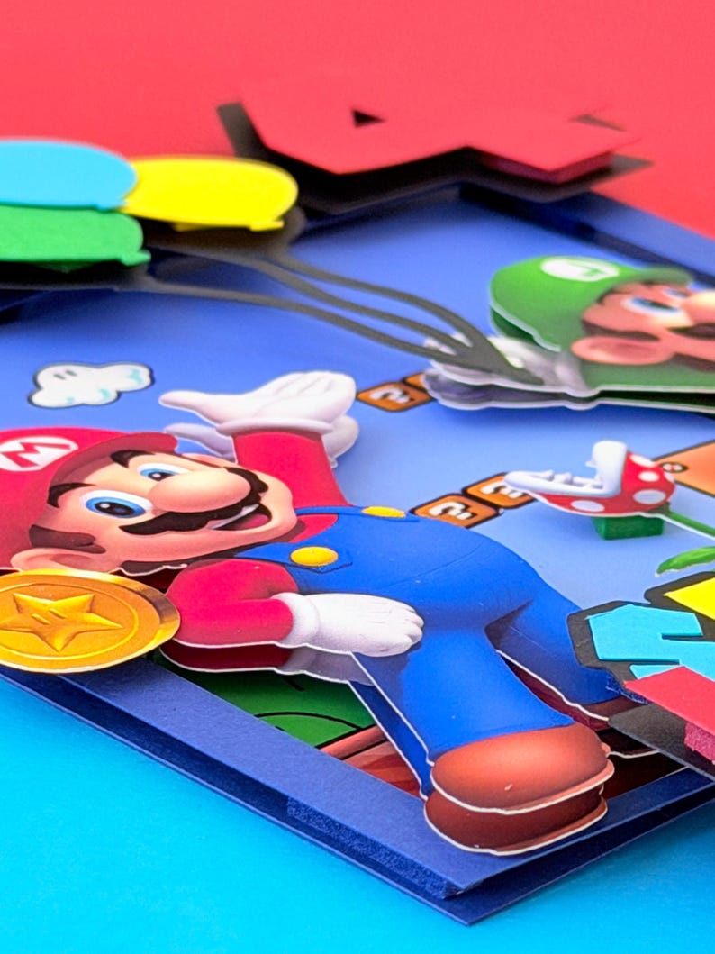 May include: A colorful, layered paper art piece featuring the character Mario from the Super Mario Bros. video game. Mario is in his signature red hat and blue overalls, with a gold coin and other game elements visible.