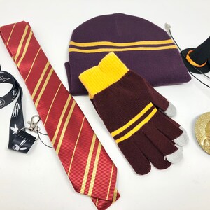 Various items are spread against a white backdrop. These include a lanyard, tie, beanie, gloves, necklace, and hair pin. The hair pin is topped with a small witch hat.