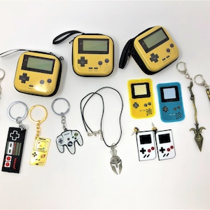 Close up of video game accessories against a white backdrop. They include coin bags in the shape of gamer consoles. There are also keychains, necklaces, earrings, and patches.