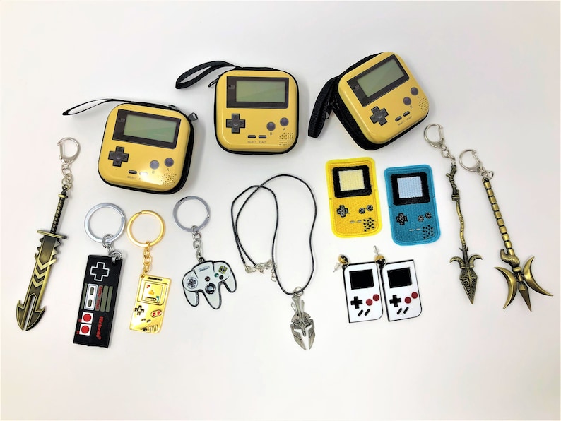 Close up of video game accessories against a white backdrop. They include coin bags in the shape of gamer consoles. There are also keychains, necklaces, earrings, and patches.