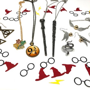 Jewelry is spread across a white backdrop with confetti. These are themed pieces for book lovers and fans of witchcraft and wizardry. They include earrings, necklaces, rings, and bracelets.