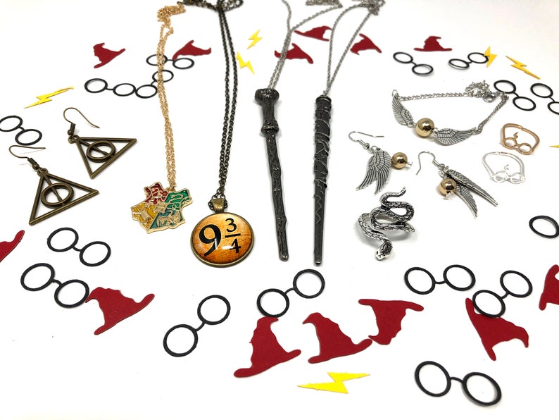 Jewelry is spread across a white backdrop with confetti. These are themed pieces for book lovers and fans of witchcraft and wizardry. They include earrings, necklaces, rings, and bracelets.