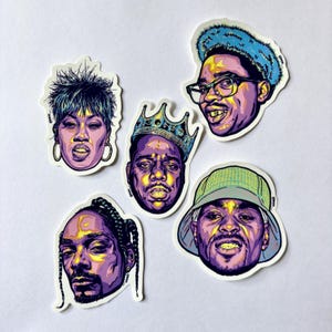 May include: A set of five stickers, each displaying a colourful, illustrated portrait of a well-known musician. The stickers are designed with bold colours and intricate details. These stickers are suitable for personalising items such as laptops, notebooks, or other belongings.