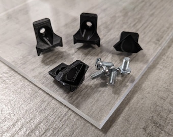 Puede incluir: Cuatro soportes de esquina de plástico negro y seis tornillos plateados. Los soportes tienen forma triangular y están diseñados para conectar dos piezas de material en un ángulo de 90 grados.