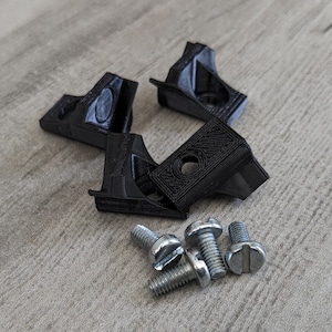 Peut inclure: Quatre équerres d'angle en plastique noir et cinq vis argentées. Les équerres ont une surface texturée et sont conçues pour relier deux pièces de bois à un angle de 90 degrés.