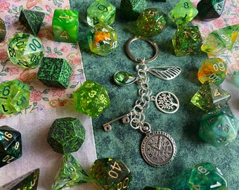 May include: A silver charm bracelet with a variety of charms, including a key, a tree, a clock, and a feather. The bracelet is surrounded by green dice with different numbers and patterns.